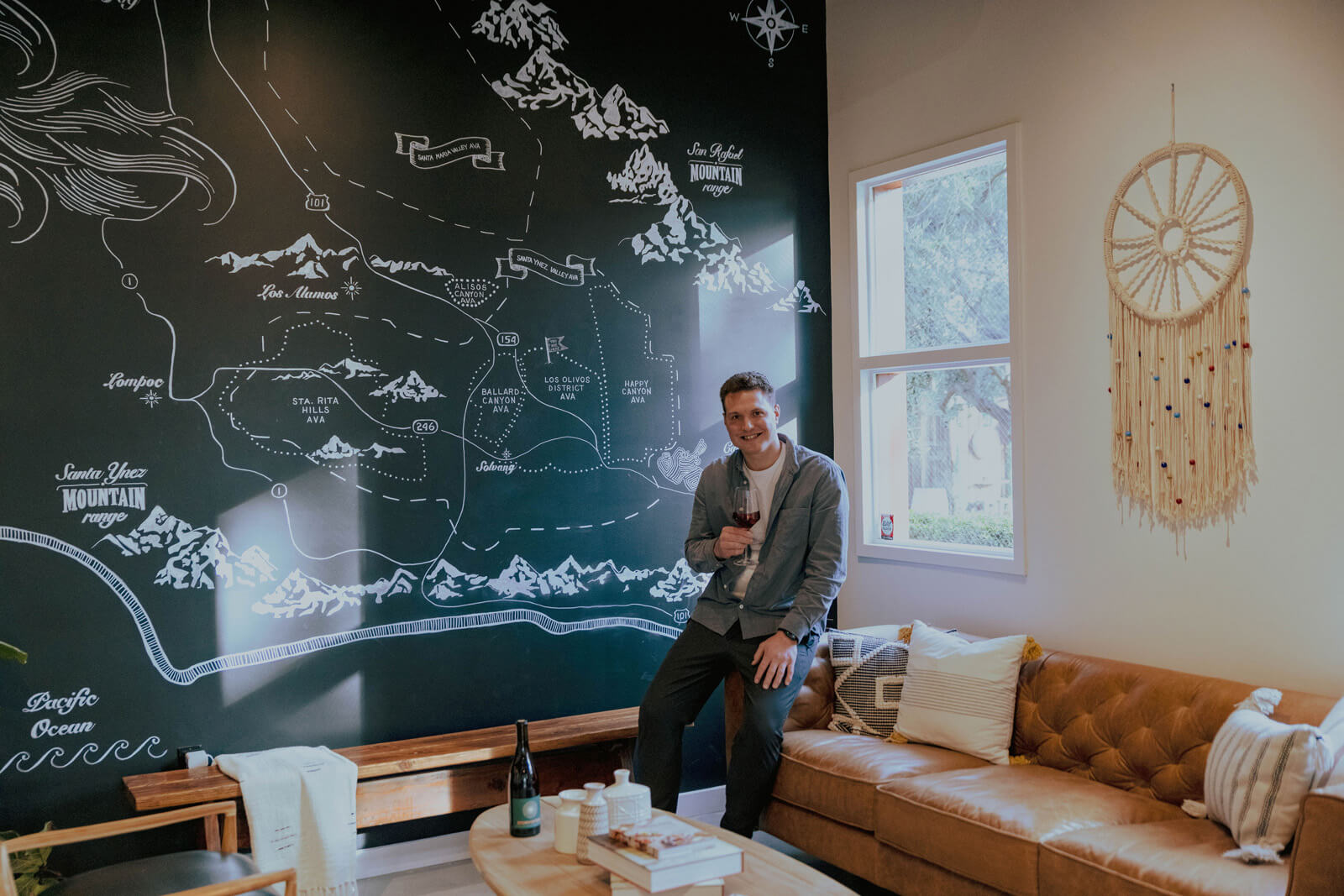 Man holding a glass of wine while seated in front of a large Santa Ynez Valley map